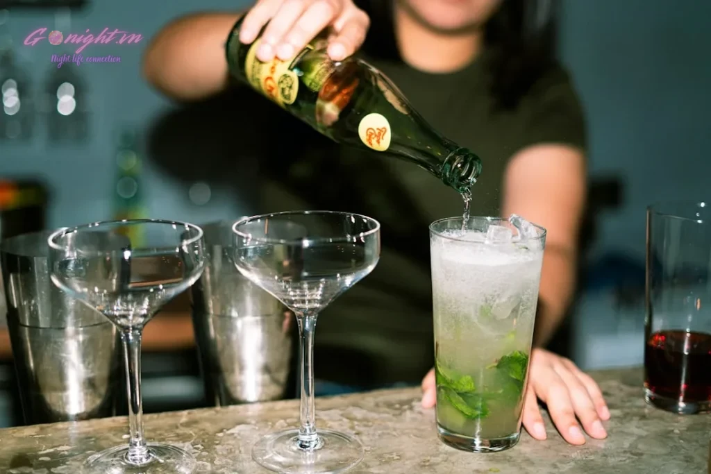 Bartender pouring drink into glass with ice and mint