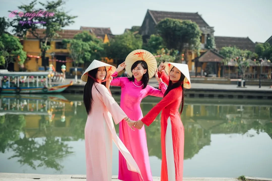 Beyond the Mic: A Comprehensive Guide to Elevating Your Karaoke Experience in Vietnam 2 Three women pose by a river in colorful attire.