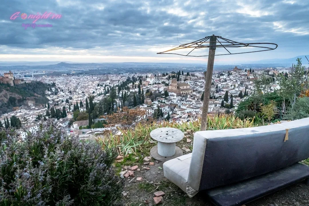 Bench and table overlook a sprawling city with distant mountains.