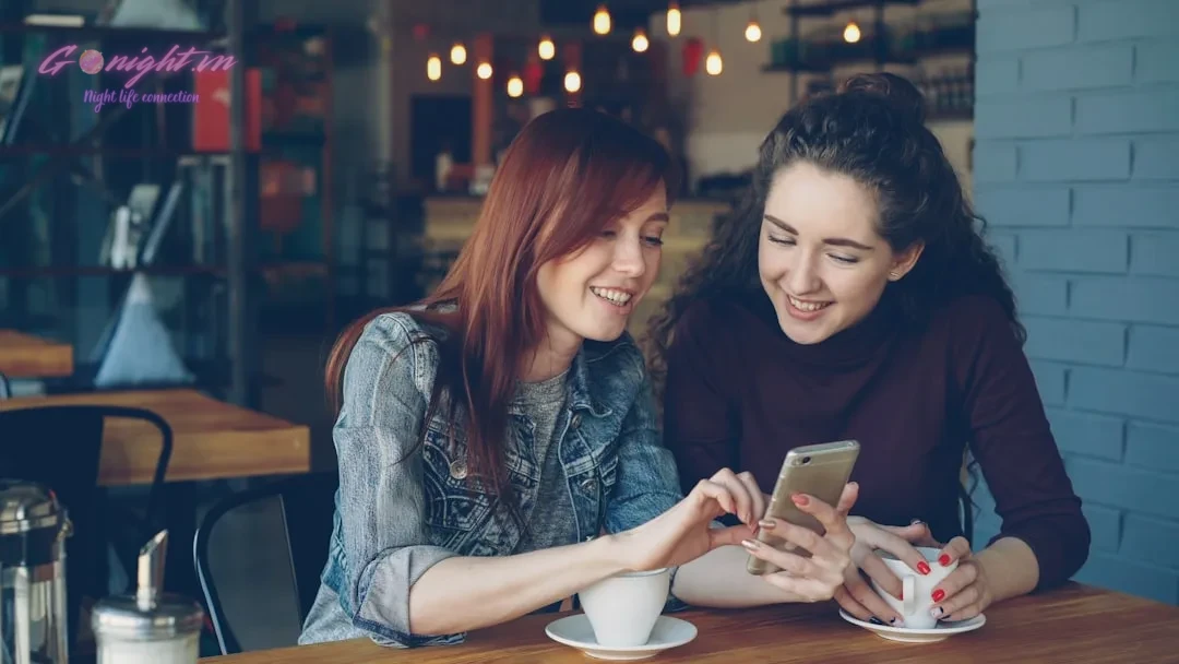 Two friends smile while looking at a phone.