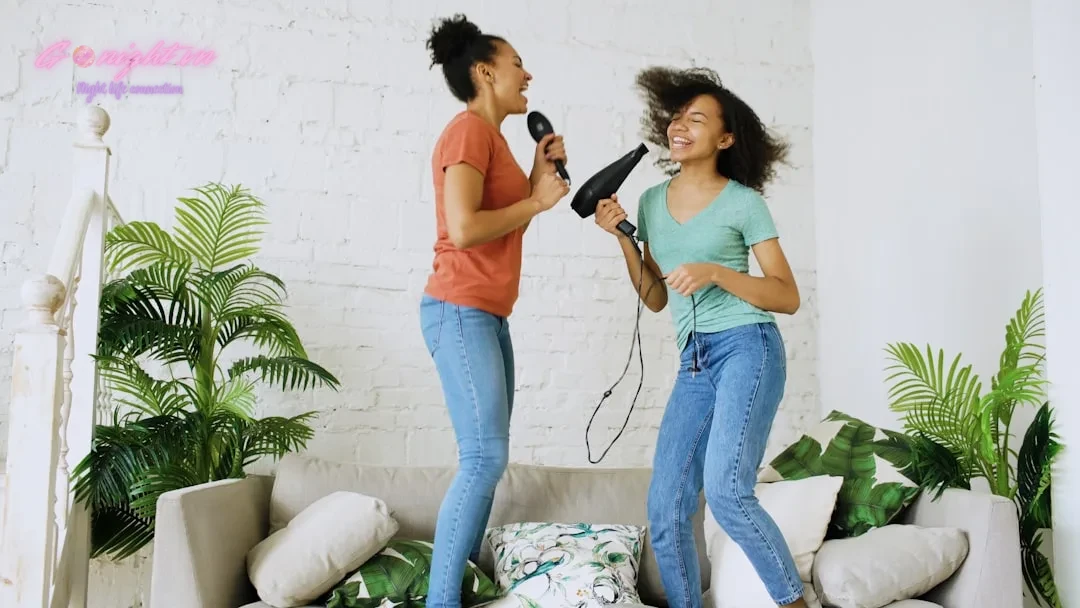Two women joyfully singing and dancing with hairdryer