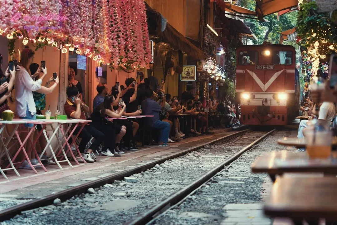 Train approaching outdoor cafe on railway tracks.