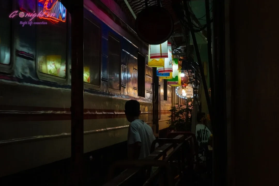 People walk past a train at night.
