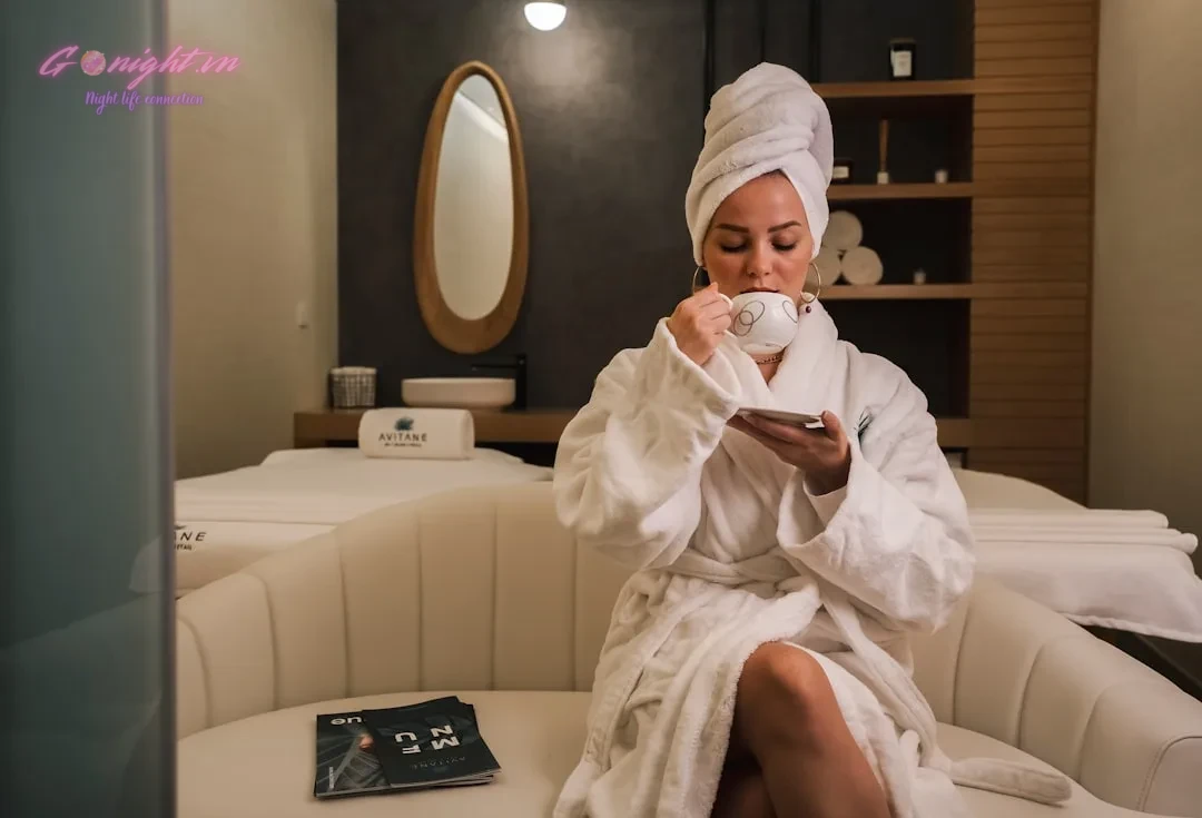Giải Mã Trải Nghiệm Massage VIP: Cẩm Nang Từ A-Z Về Gói Dịch Vụ, Tip Bo Tinh Tế & Chọn Đúng Gu Thư Giãn 9 woman in white robe sitting on white couch