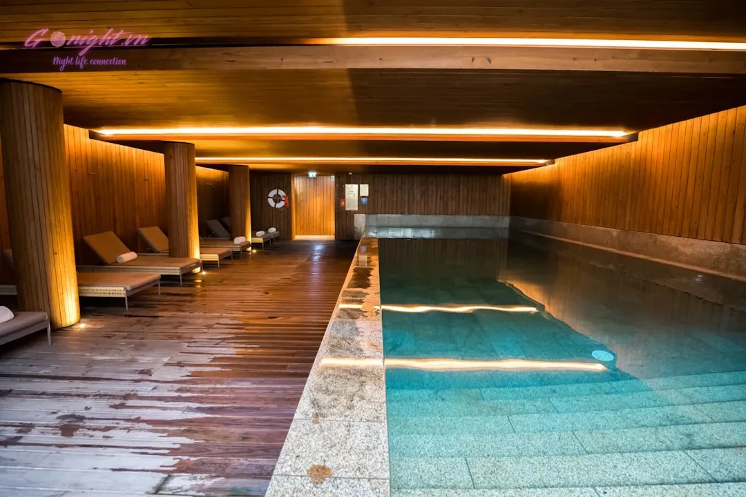 Indoor swimming pool with wooden walls and lounge chairs.